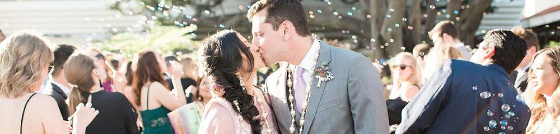 bride and groom kiss as wedding guests blow bubbles