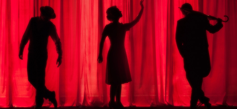 silhouette of three actors against a red curtain