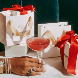 close up of a hand holding a cocktail in front of gift bags