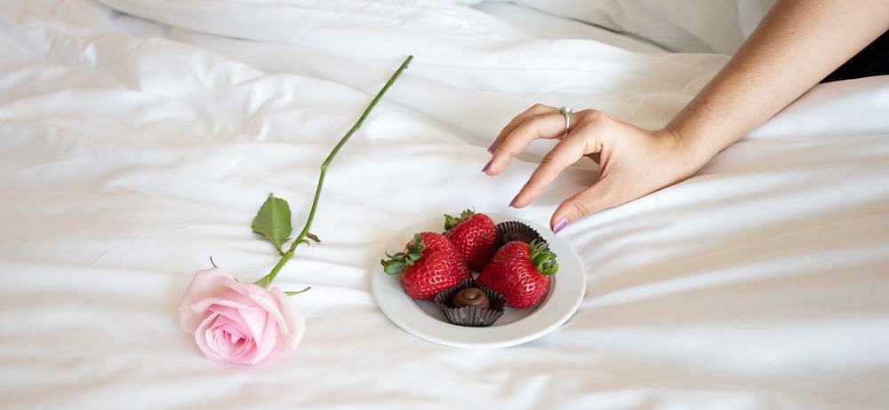 plated strawberries and chocolate and a pink rose on a bed
