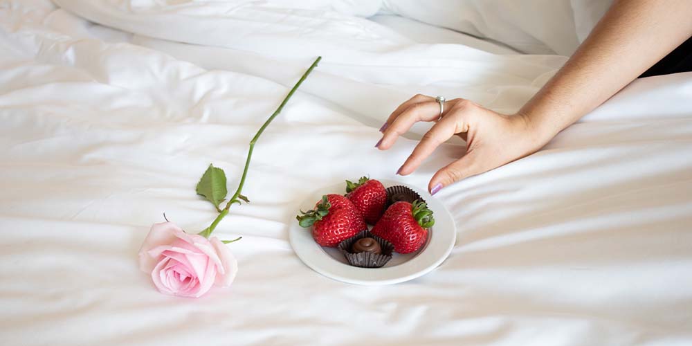 plated strawberries and chocolate and a pink rose on a bed