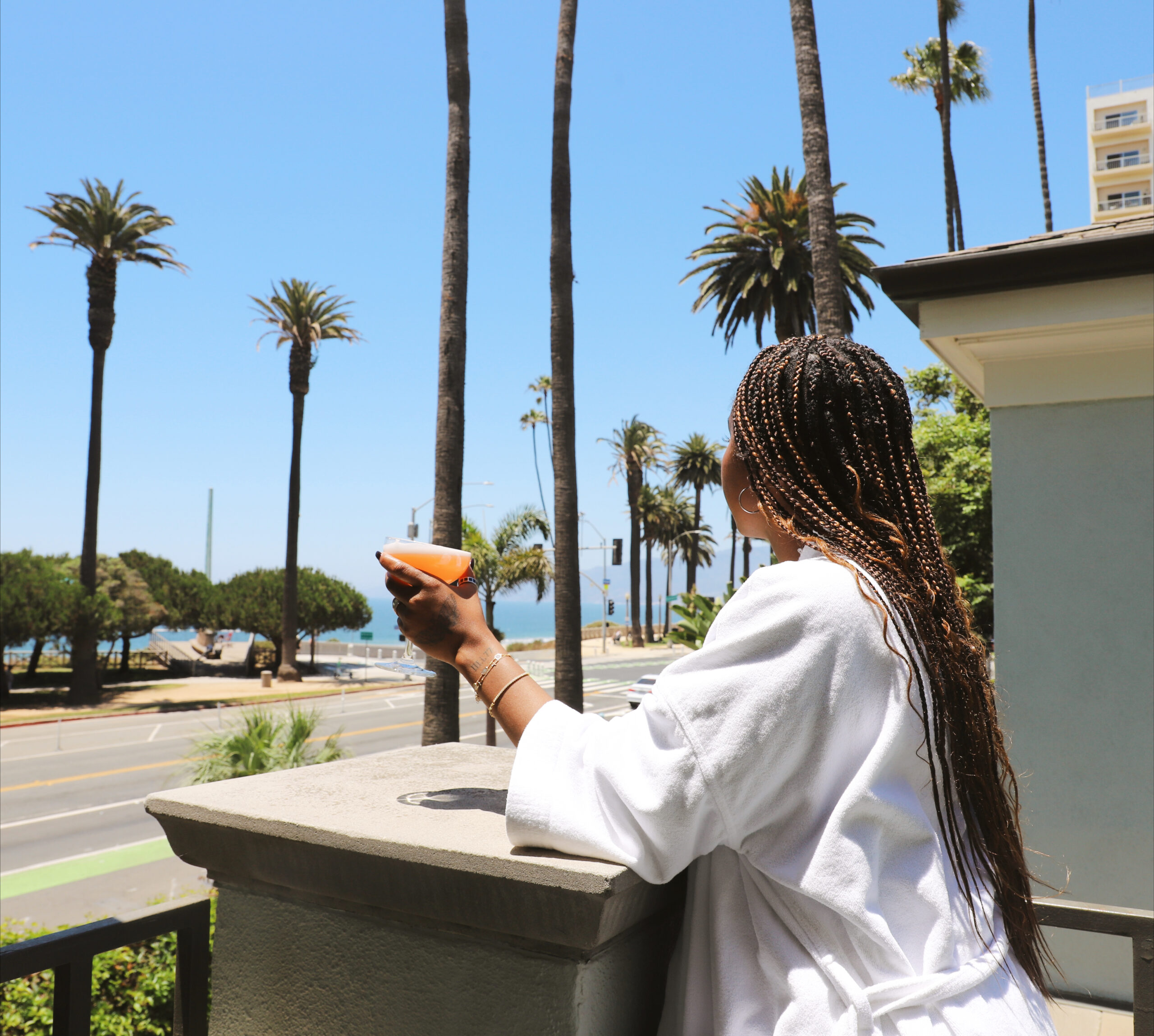 woman in bathrobe drinking a cocktail on a balcony