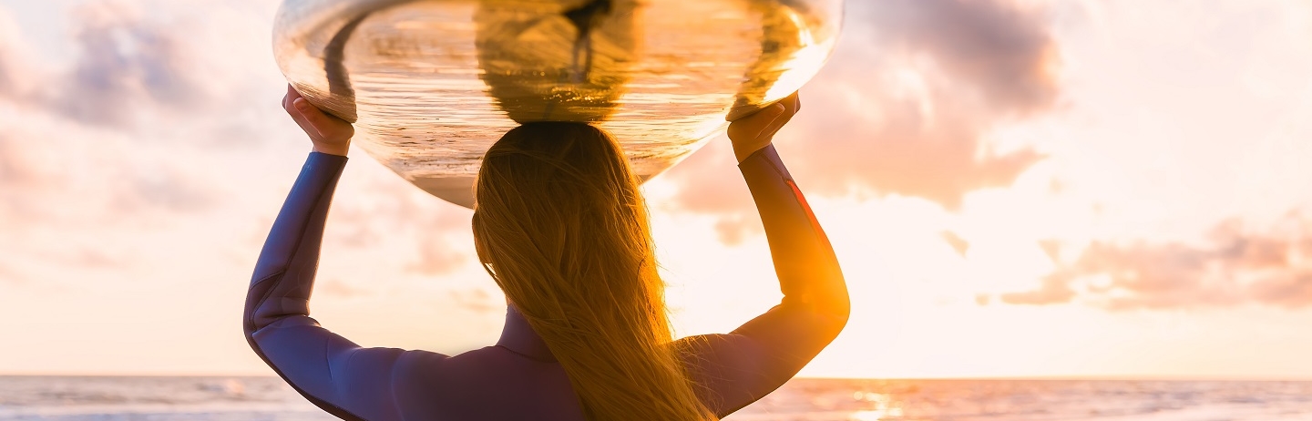woman with surf board resting on head looking out at the sunset
