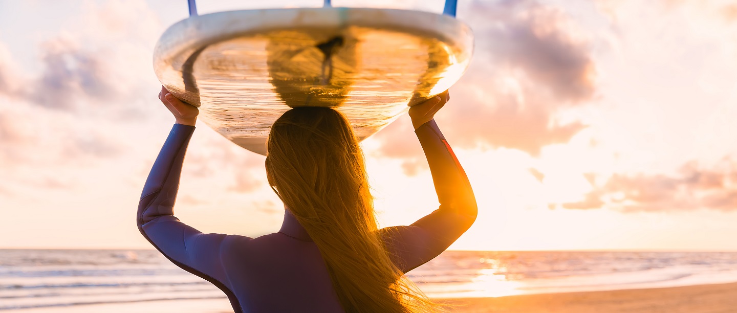 woman with surf board resting on head looking out at the sunset