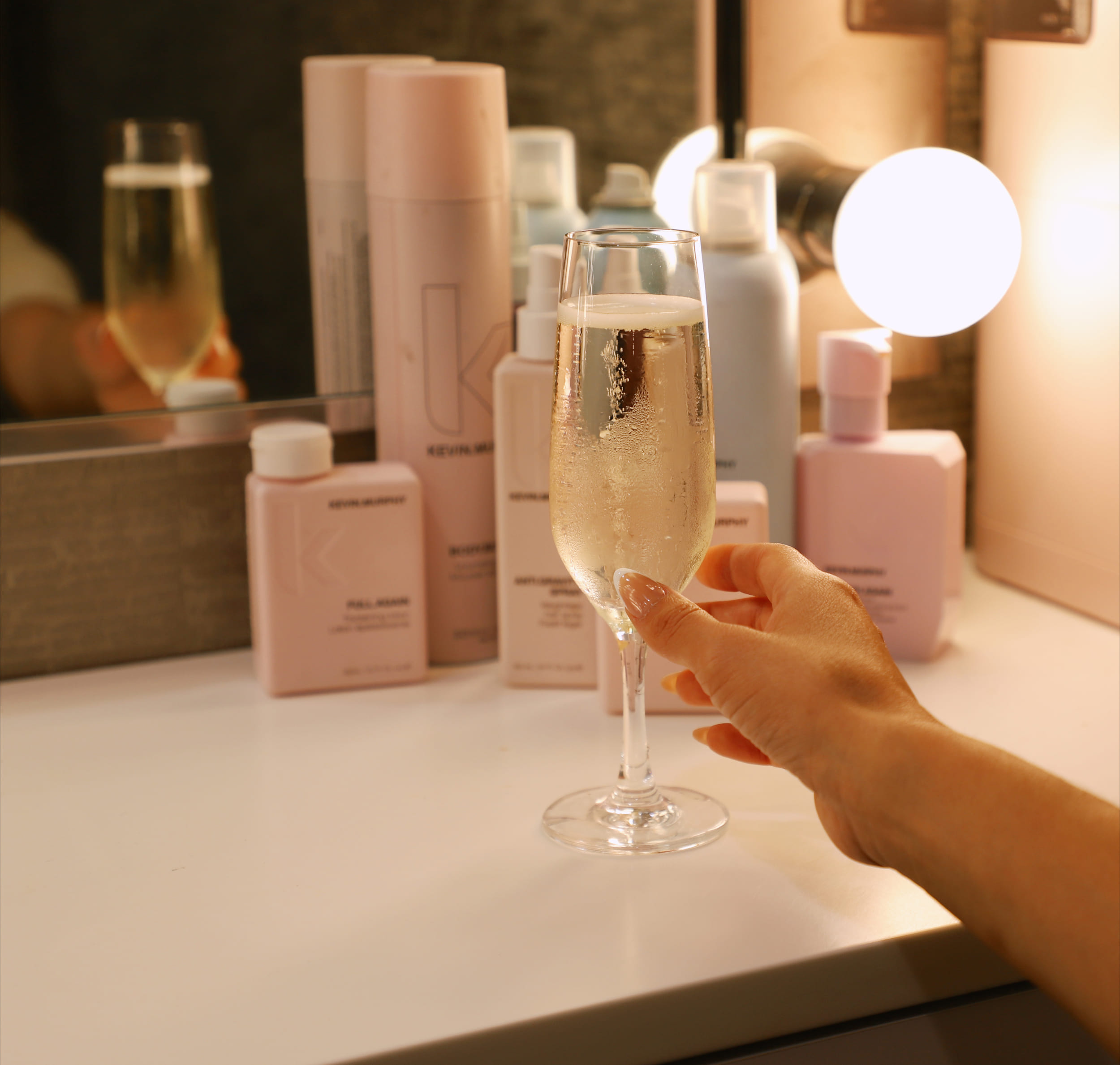 someone picking up a glass of champagne with salon products in the background