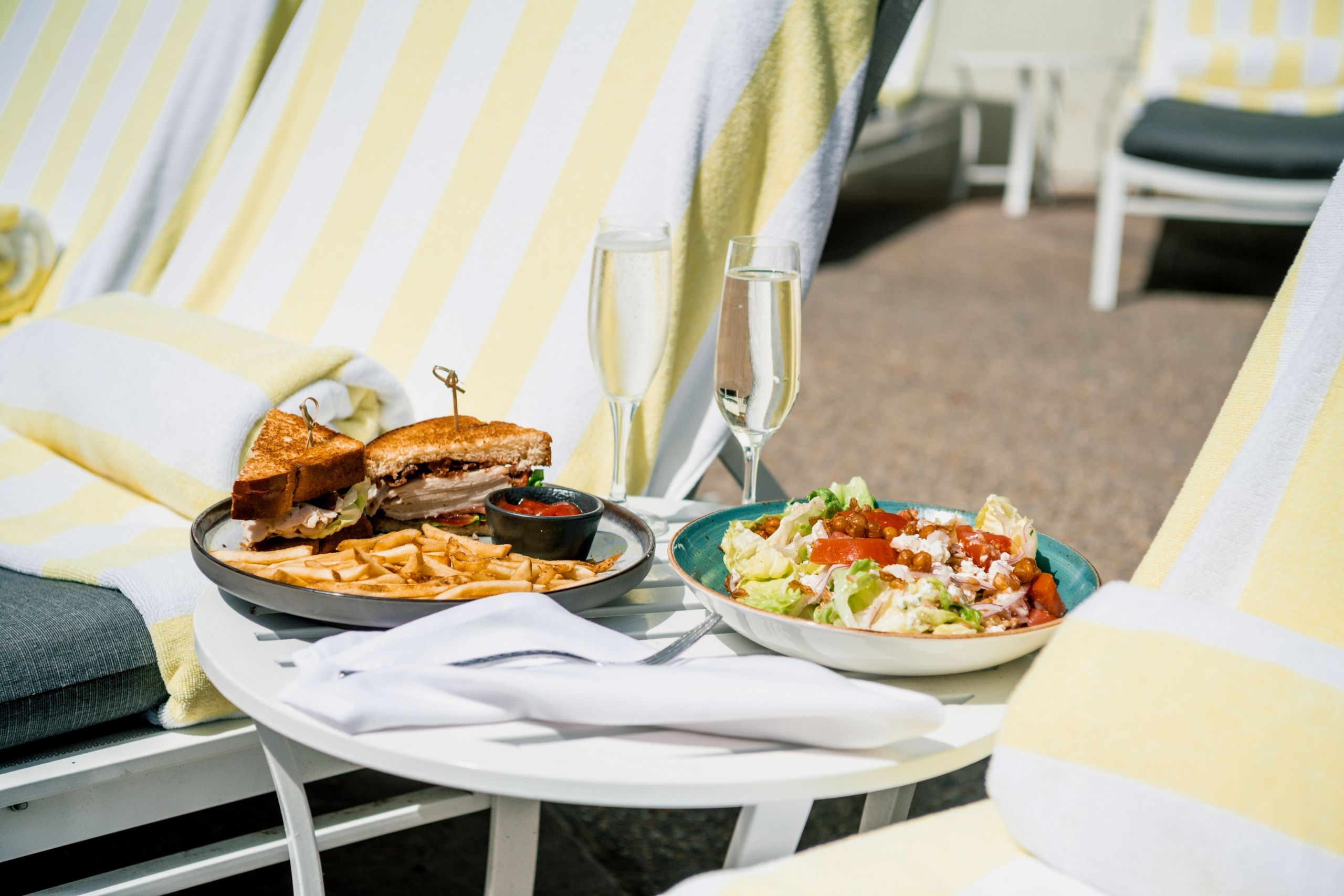 sandwich and salad on poolside table with two loungers